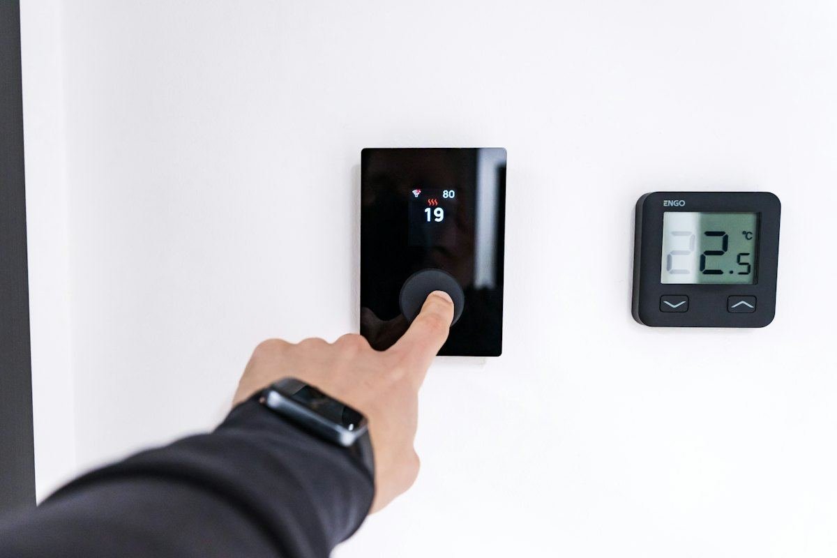 A finger adjusting a modern digital thermostat on a white wall