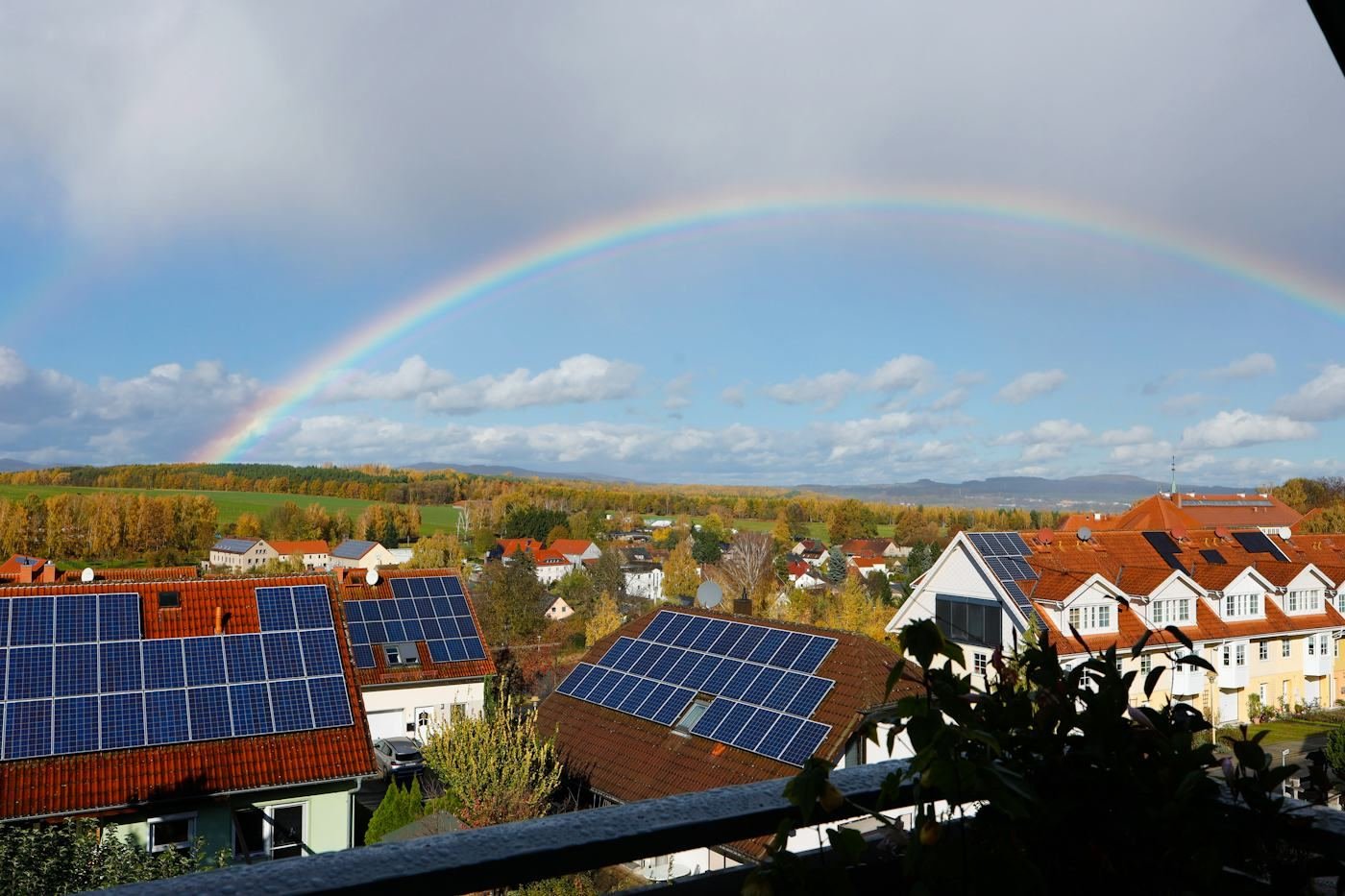 Rooftop solar panels on a hillside of houses under a rainbow